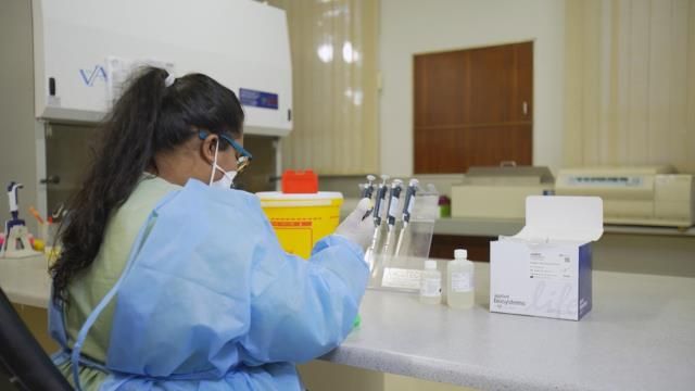 A lab worker in protective gear uses pipettes at a laboratory bench. 