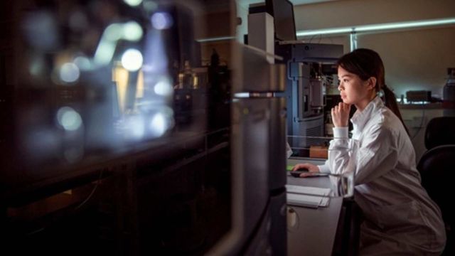 Laboratory researcher analyzing data at computer workstation in modern science lab. 