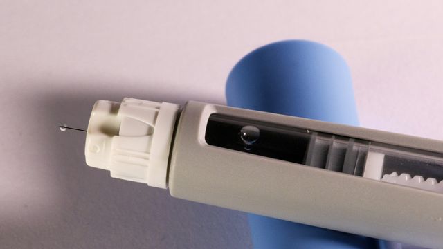 Exposed needle on an auto-injector device, balanced on top of the removed blue cap. 
