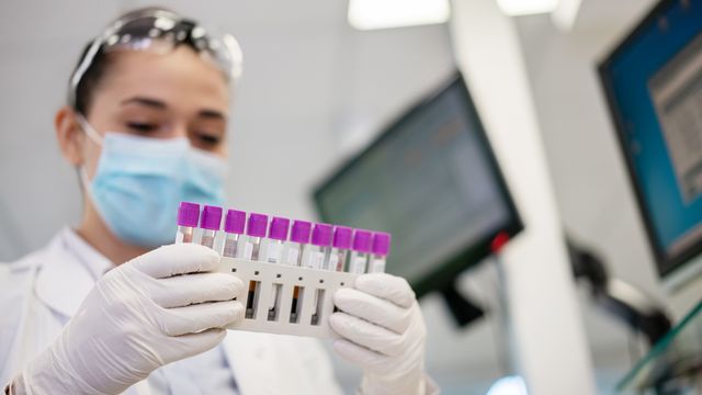 Lab technician holding rack of purple-capped biosamples in test tubes. 