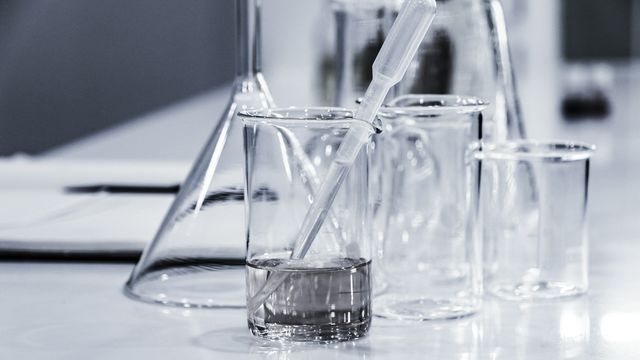 Laboratory beakers and pipette with clear liquid on a clean lab bench. 