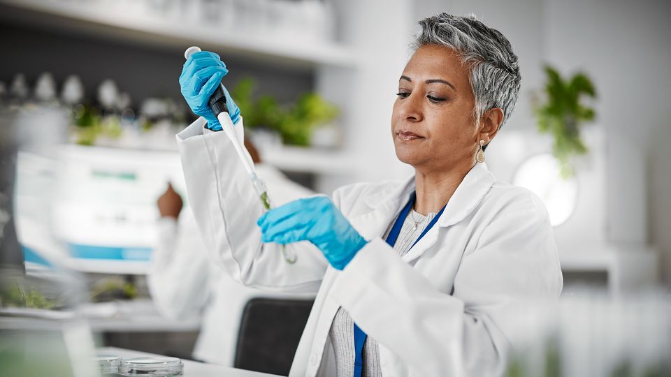 A woman in a lab coat and blue gloves using a pipette in a research laboratory.