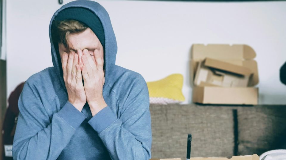 Young man in a hoodie covering his face with hands, showing stress or fatigue.