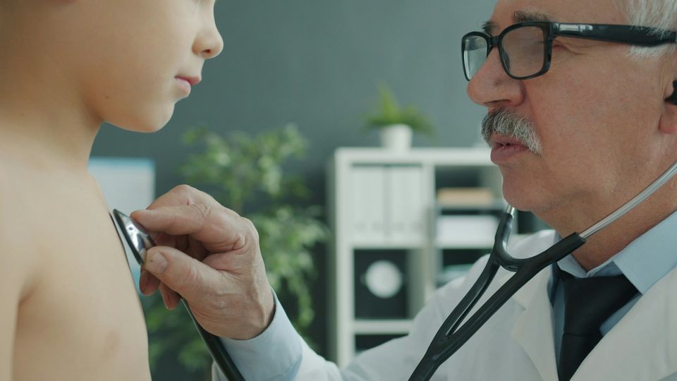 Doctor using a stethoscope to examine a pediatric patient's chest, in a clinical setting.