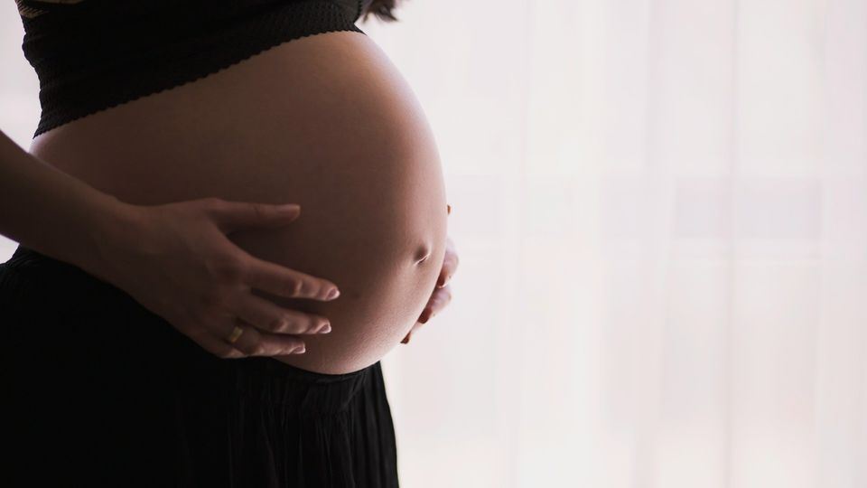 Close-up of a pregnant woman holding her baby bump.