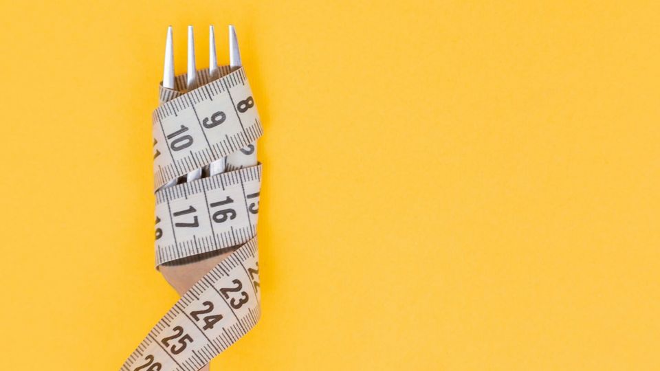 Fork wrapped in measuring tape on yellow background.