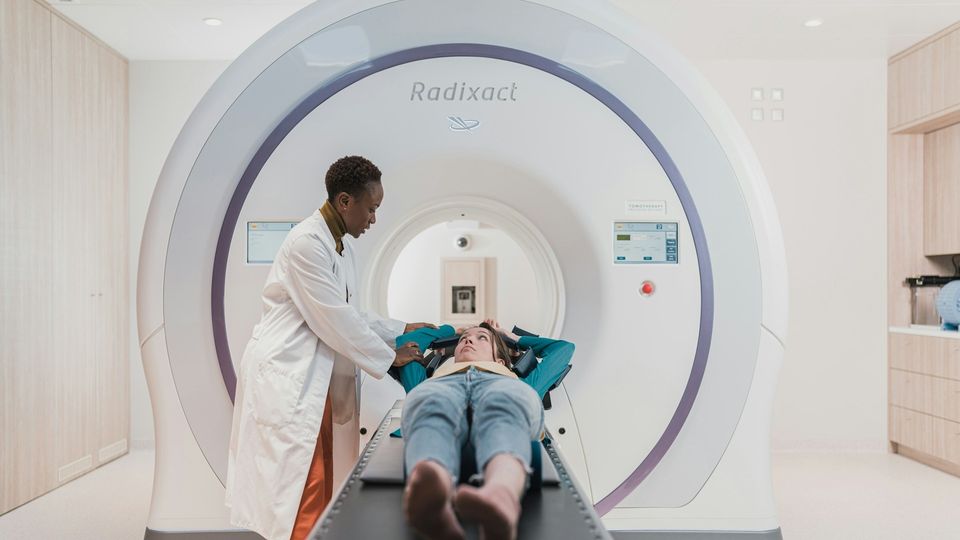 Patient undergoing MRI scan while technician positions them in a medical imaging machine.