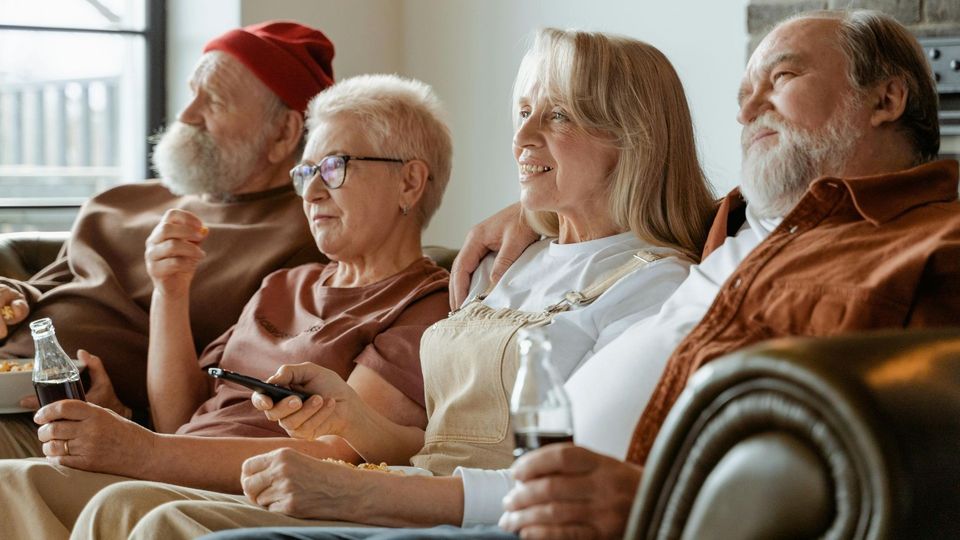 Group of older adults relaxing on a couch, and watching TV.