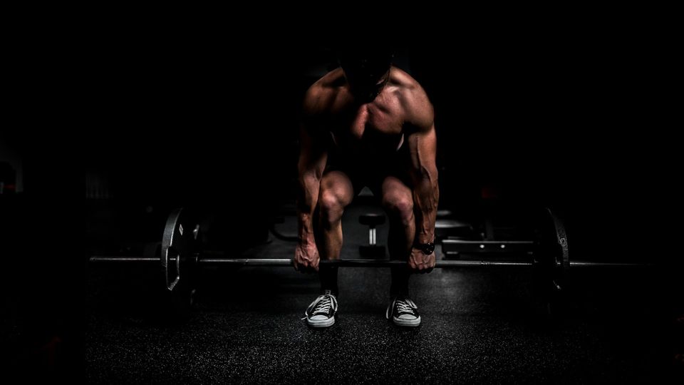 Bodybuilder performing a deadlift with barbell in a dark gym.