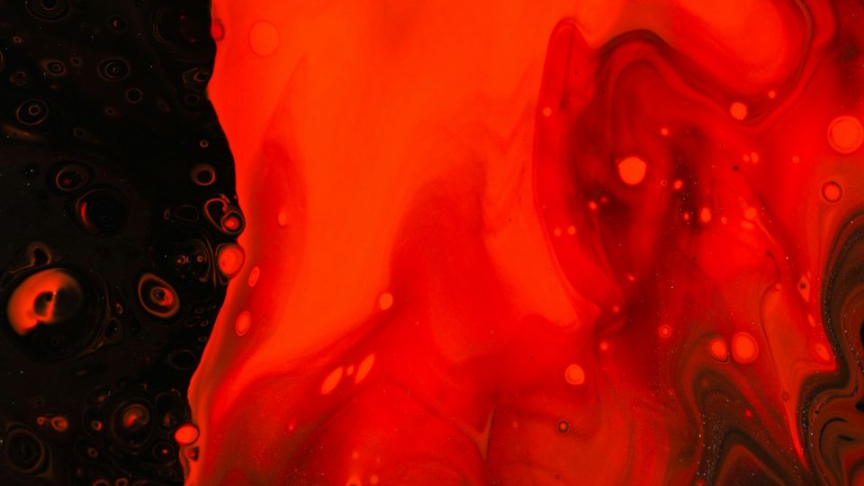 Birds-eye view of red liquid flowing across a black surface.