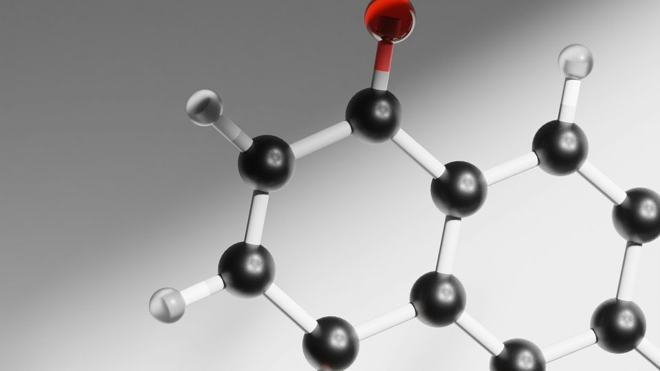 Close-up of a 3D molecular structure model showing atoms in black, gray, and red, with bonds linking them together.