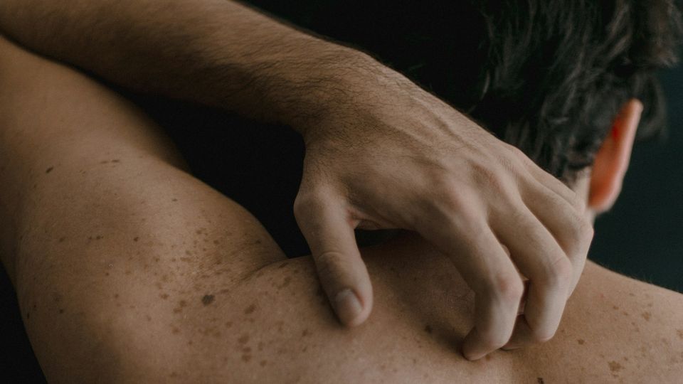 Close-up of a mans hand as he scratches his back.