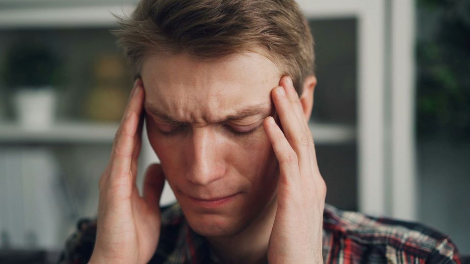 Young man holding temples with his eyes closed, grimacing in pain.