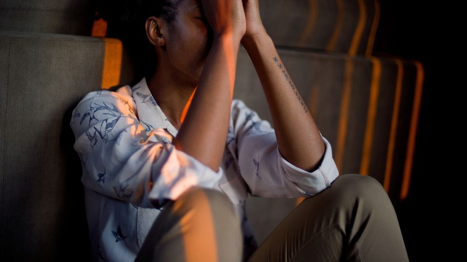 Person sitting beside a wall with hands covering face.