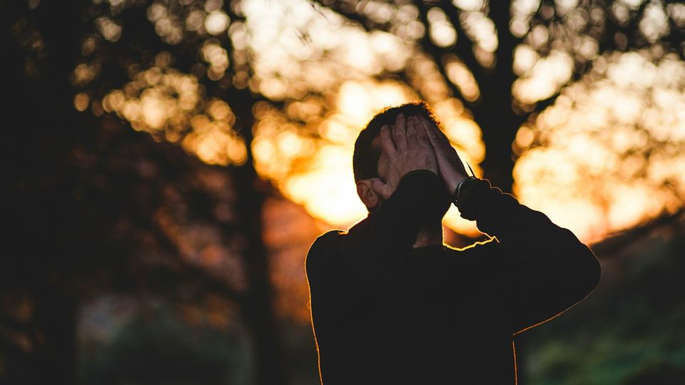 Man covering his face outdoors at sunset.