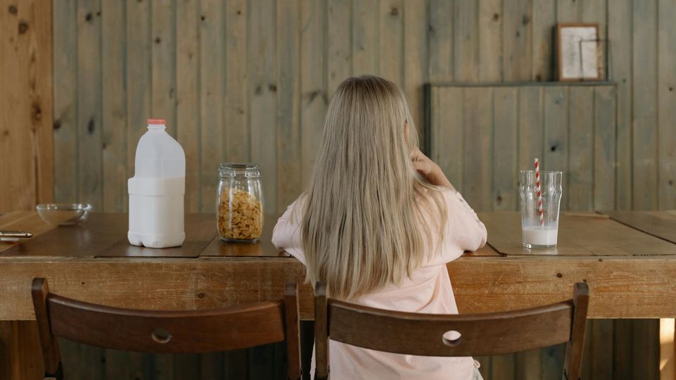 A young girl sitting at a dining room table, with a milk bottle and a half-full glass of milk beside her.