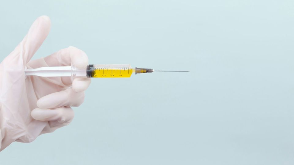 Gloved hand holding a syringe with yellow liquid for medical injection.