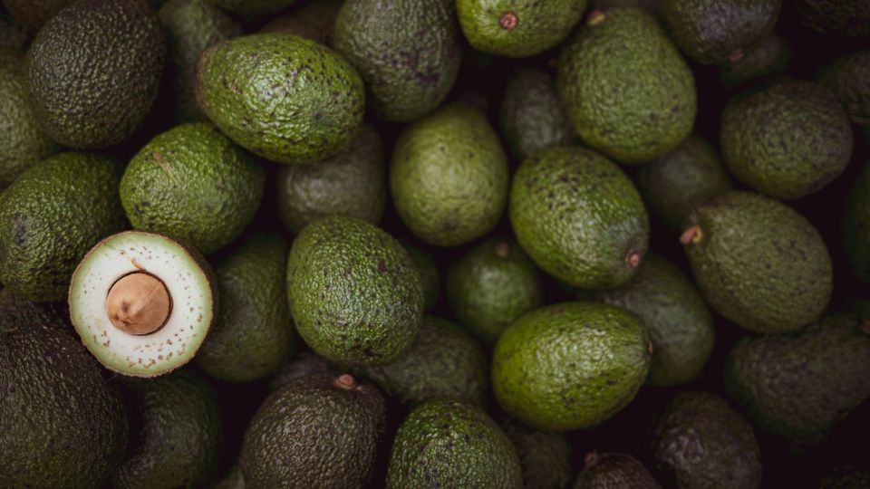 Fresh avocados with one cut open showing seed and creamy green flesh.