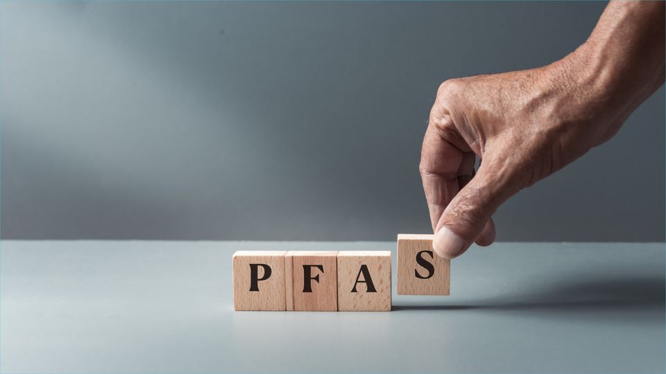 A hand placing down four wooden letter blocks, spelling out "PFAS".