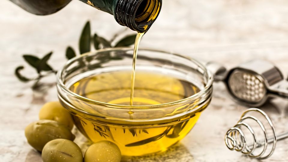 Pouring olive oil into a glass bowl, with olives and kitchen tools nearby.