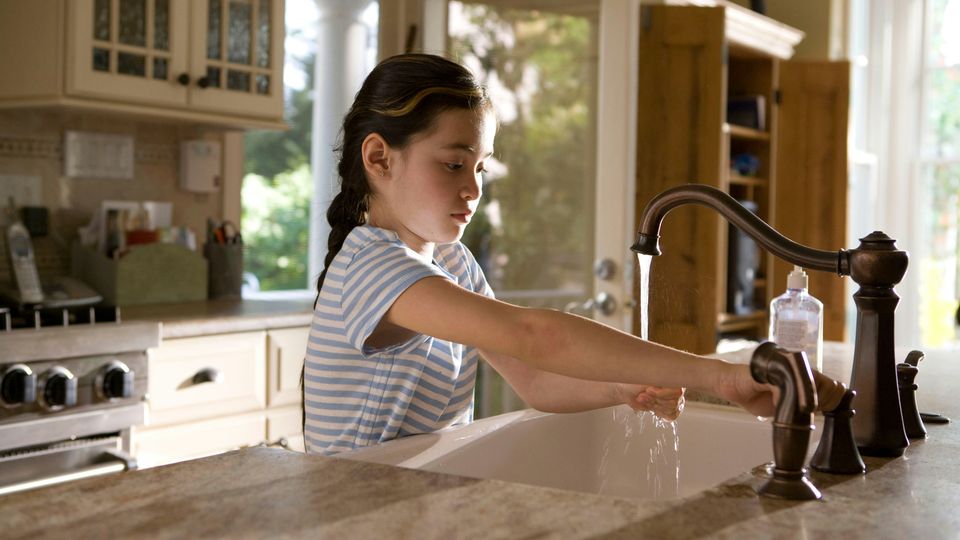 A young girl turning on the tap at a kitchen sink.