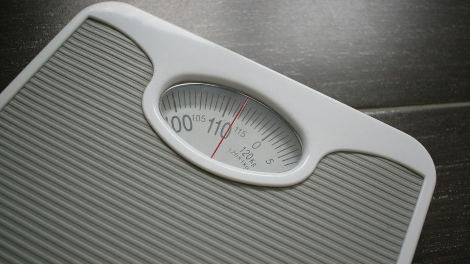 Birds-eye view of a white and gray analog weighing scale placed on a dark flooring.