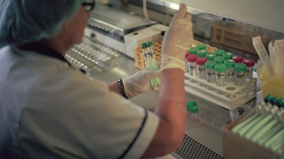 Researcher handling sample tubes in a laboratory biosafety cabinet.