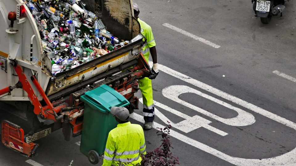 Garbage truck collecting waste with sanitation workers on a city street.