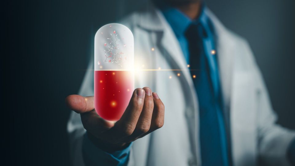 Doctor wearing a lab coat with an outstretched hand holding a glowing red and white oversized drug capsule. 