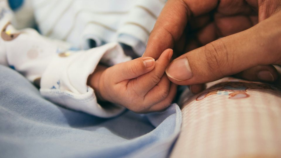 Close-up of a newborn baby holding an adult’s finger.