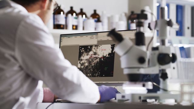 Scientist analyzing cellular data on computer with microscope in transcriptomics lab. 