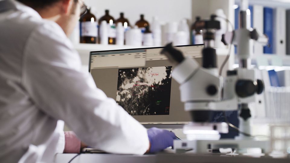 Scientist analyzing cellular data on computer with microscope in transcriptomics lab.