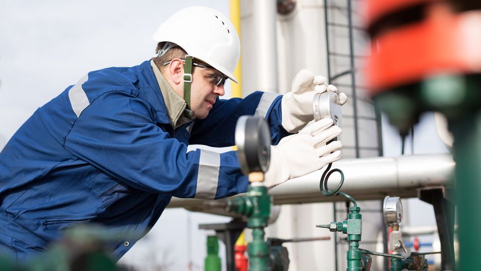 A gas engineer inspecting some pressure gauges on a large segment of piping.