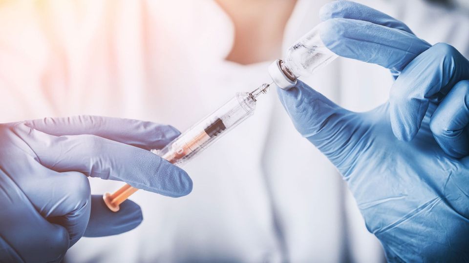 Close-up of gloved hands drawing vaccine liquid from a vial into a syringe.