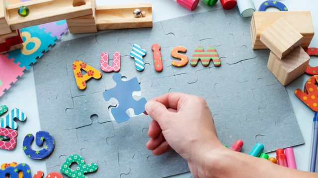 Colorful puzzle pieces spelling autism with hand placing piece, symbolizing autism awareness. 