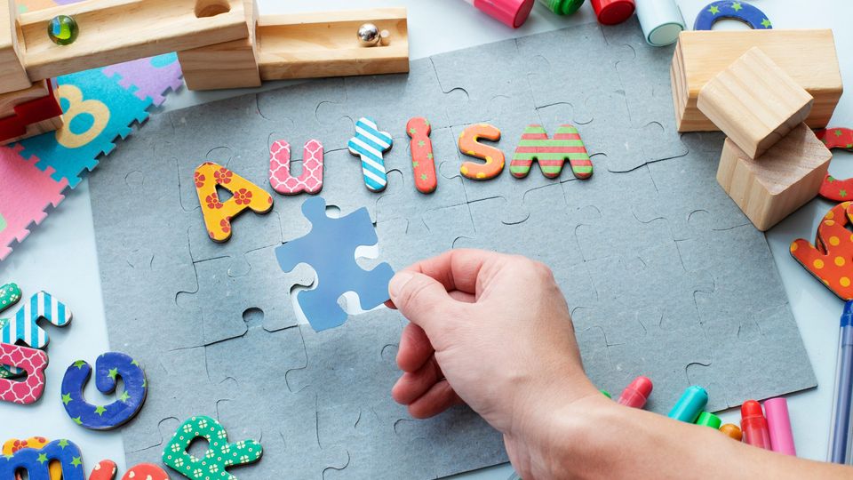 Colorful puzzle pieces spelling autism with hand placing piece, symbolizing autism awareness.
