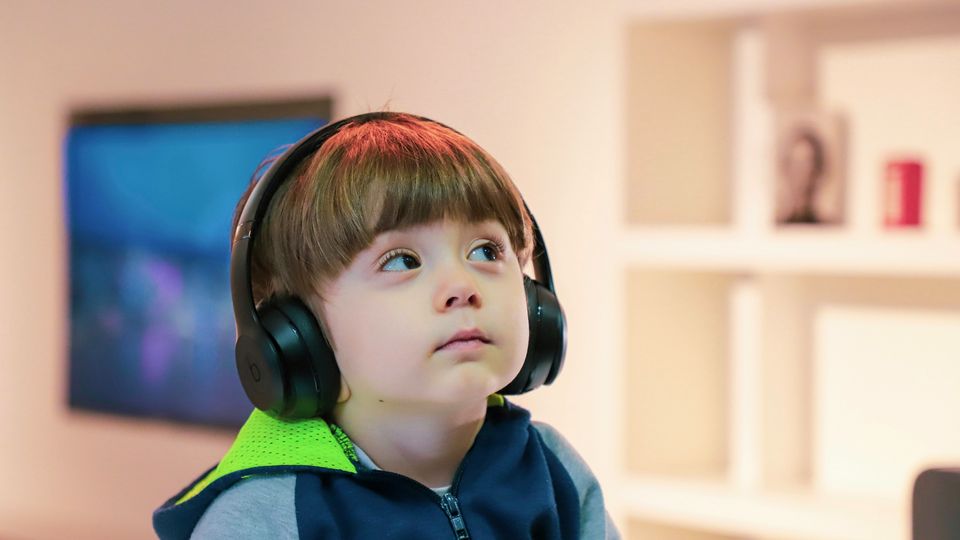 A young boy avoids eye contact while wearing over-ear headphones, representing autistic traits.