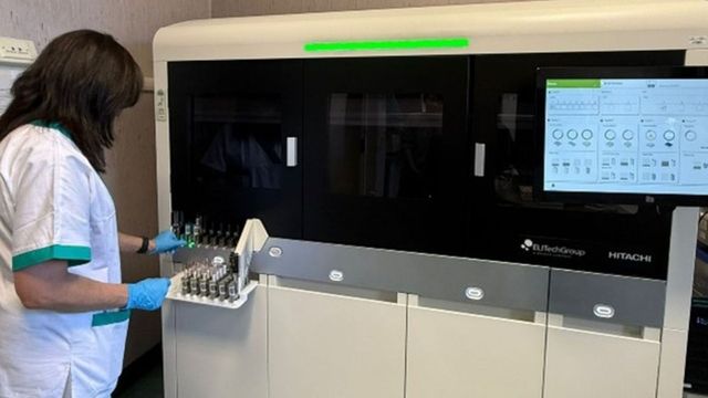 Laboratory technician loading sample vials into automated diagnostic analyzer machine. 