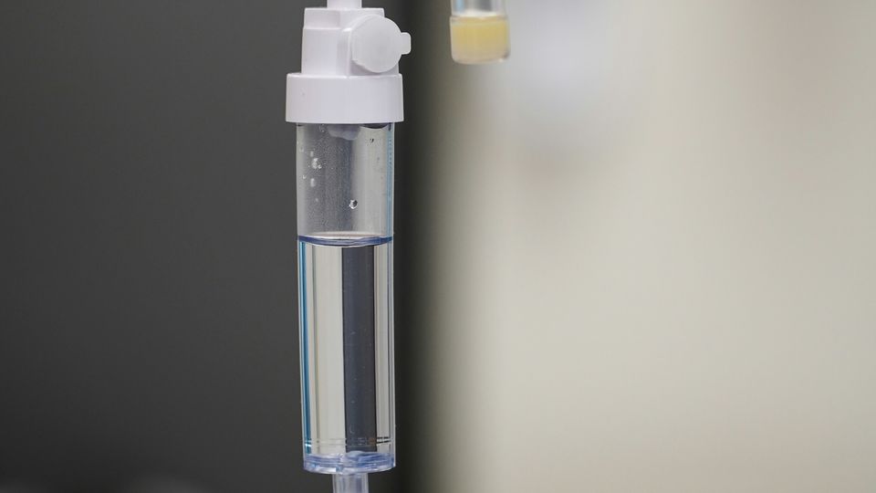 Close-up of a hospital drip set-up, containing clear fluid, against a light background.