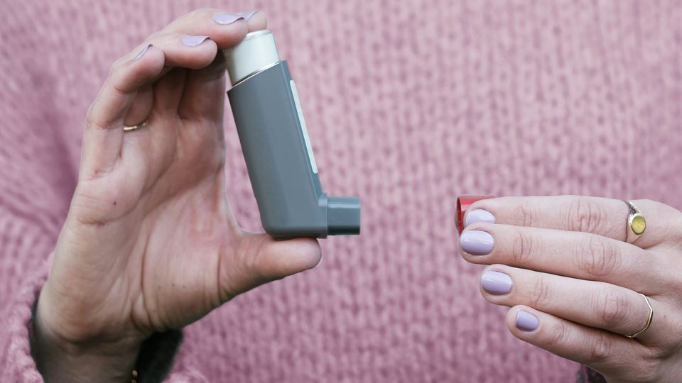 A woman removing the cap from a gray asthma inhaler.