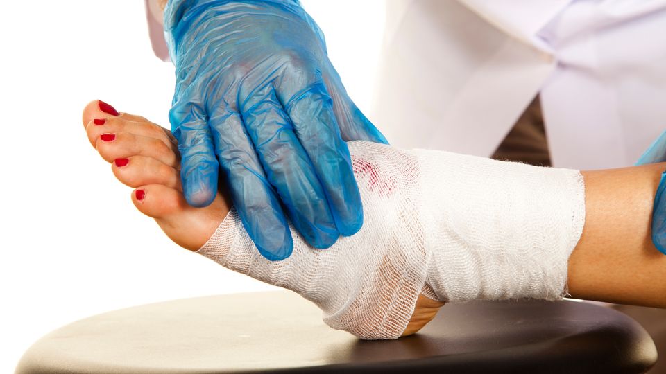 The gloved hand of a doctor applies a bandage to a wound on a foot.