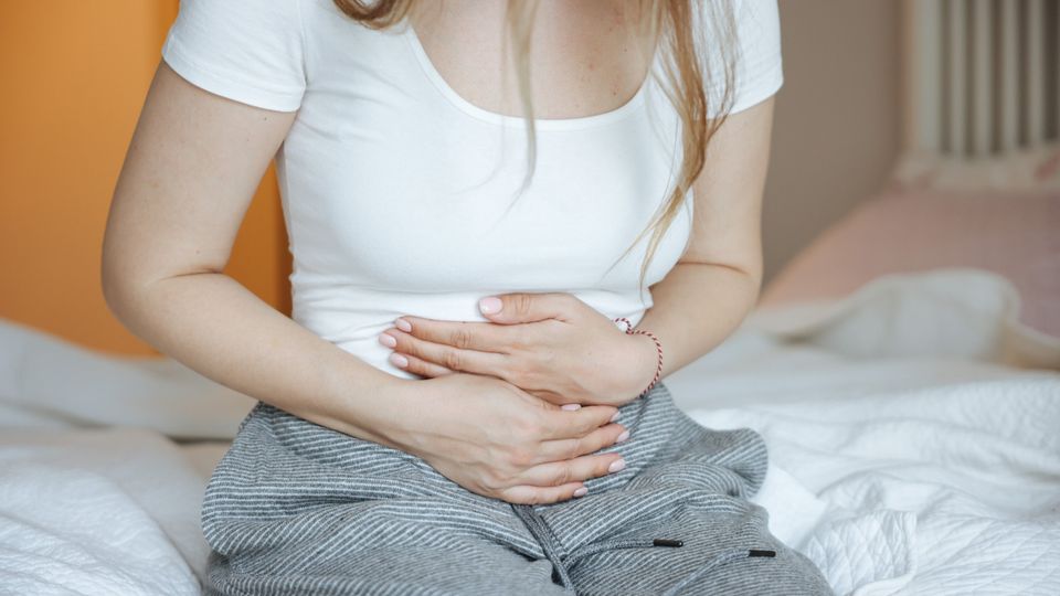 Person holding abdomen in discomfort while sitting, illustrating chronic pain.