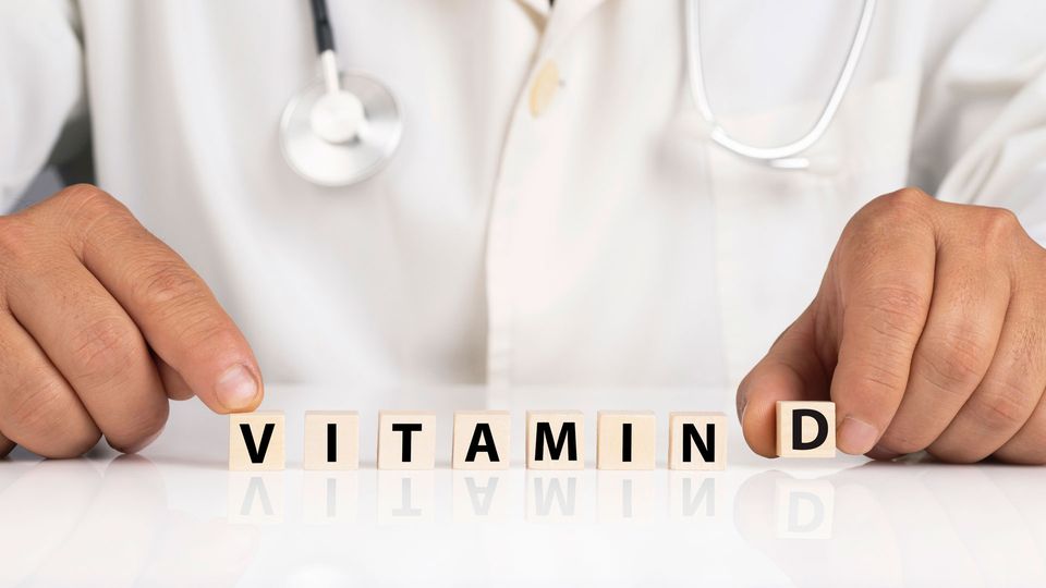 Doctor arranging “vitamin D” letter blocks on table, illustrating vitamin D health concept.
