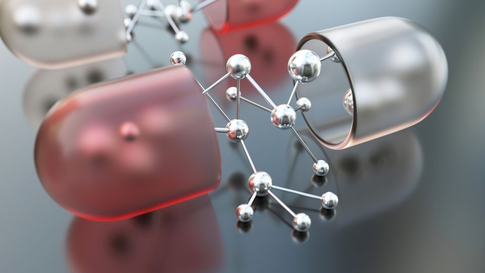 Red and white medicinal capsule cut in half with a silver ball and stick molecular model in the middle.