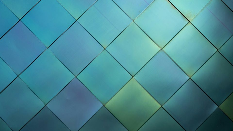 Iridescent metallic tiles on building facade in blue-green gradient pattern.