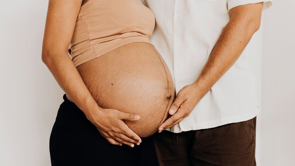 Mid-section of a pregnant person and partner with their hands placed on the baby bump.