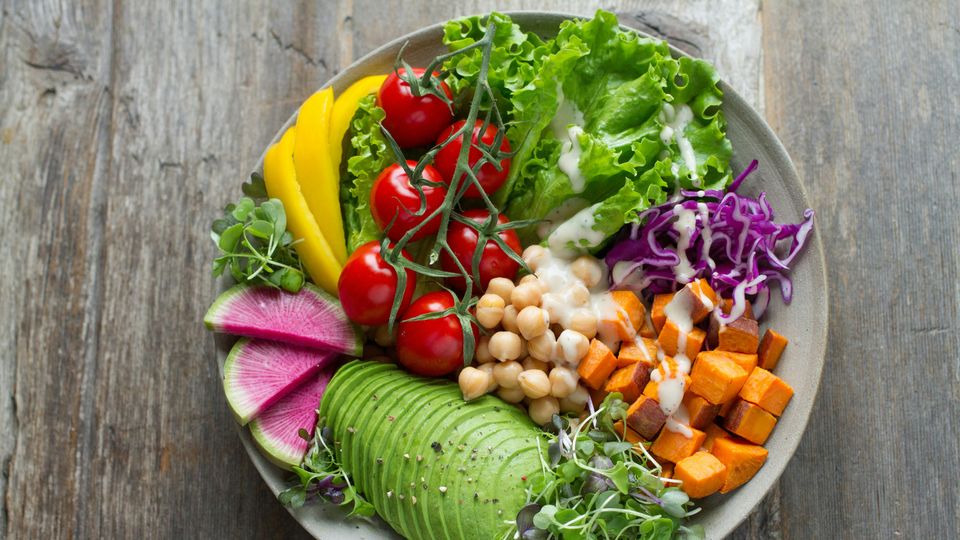 A large plate of salad, featuring a mixture of vegetables, leafy greens, and cubed sweet potato.