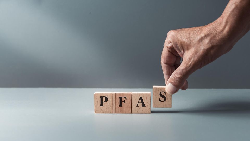 Hand placing wooden blocks in a row to spell the word "PFAS". 
