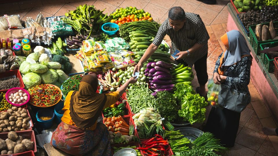 Fresh vegetables and shoppers at a busy local produce market.