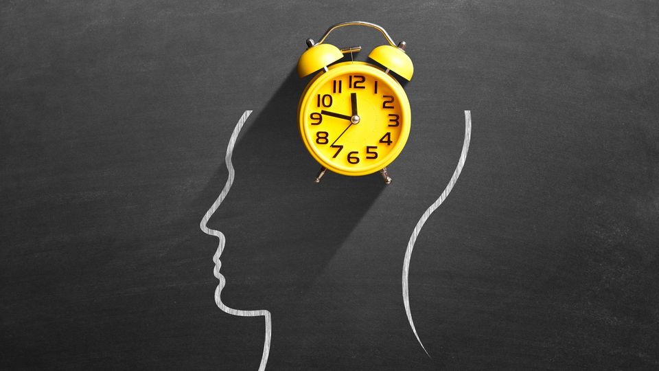 Yellow alarm clock above chalk outline of a head, symbolizing time perception and mental awareness.